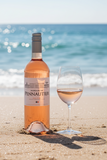 A bottle of Marquis de Pennautier Pays d'Oc white wine, showing the pale pink liquid through the clear glass bottle with a white and silver label and cap.